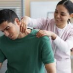A smiling therapist performs massage therapy on a man's sore neck to help relieve painful pinched nerve tension and discomfort.